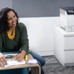 Xerox® VersaLink® C620 printer in an office Smiling woman in an office next to the Xerox® VersaLink® C620 Colour Printer