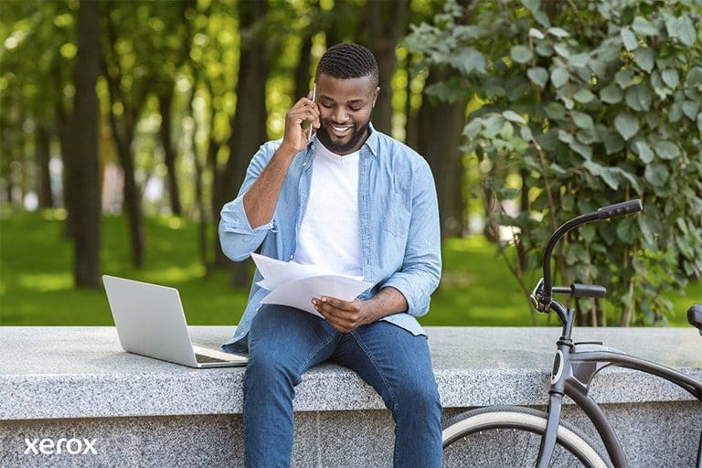 A man is seated on a bench, using his laptop, while his bicycle is parked next to him in a peaceful environment. A man is seated on a bench, using his laptop, while his bicycle is parked next to him in a peaceful environment.